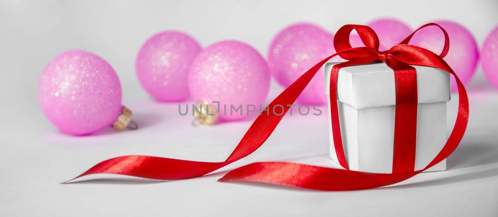 Christmas Gift in White Box with Red Ribbon and Pink Balls on Light Background. New Year Holiday Composition Banner. by Svetlana_Belozerova