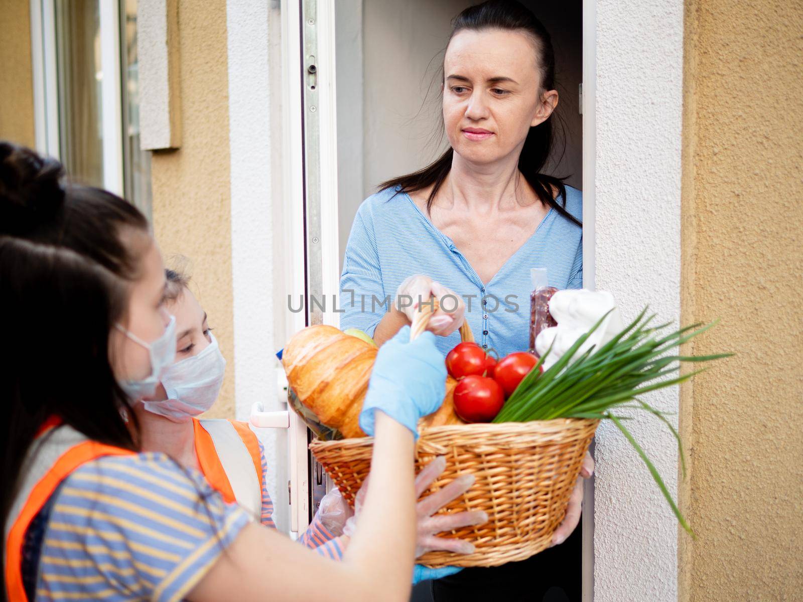 Teenage girls volunteers in protective masks and gloves deliver food to poor people.