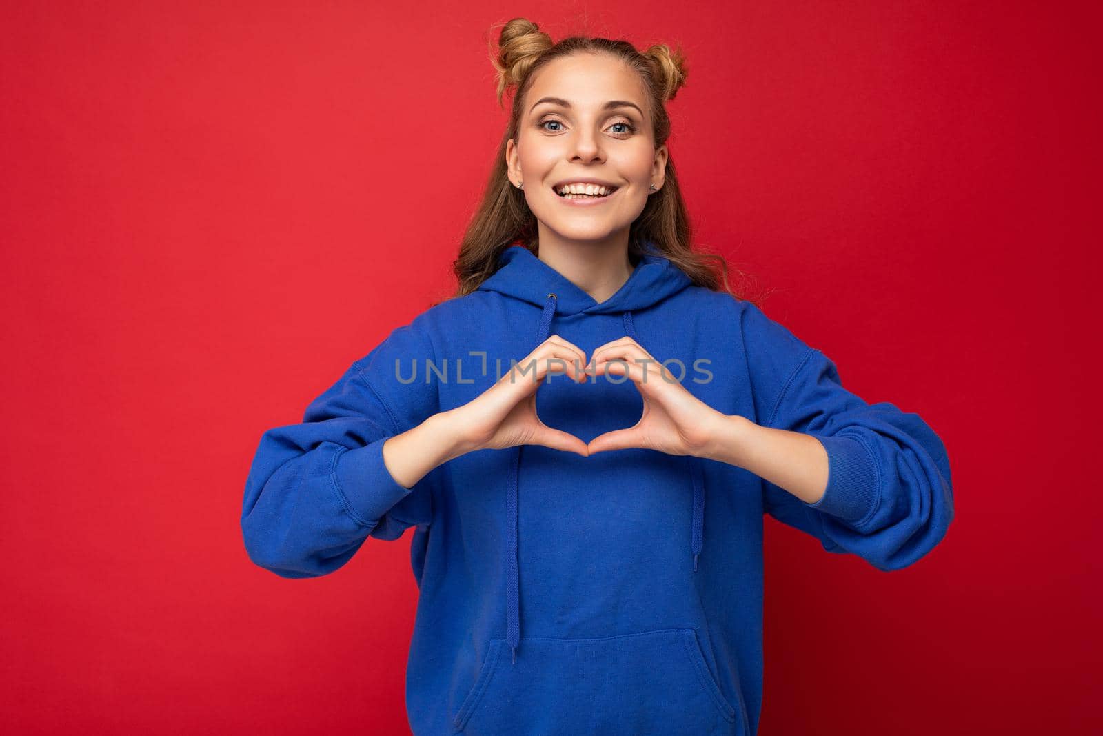 Photo of young positive happy smiling beautiful woman with sincere emotions wearing stylish clothes isolated over background with copy space and showing heart gesture by TRMK