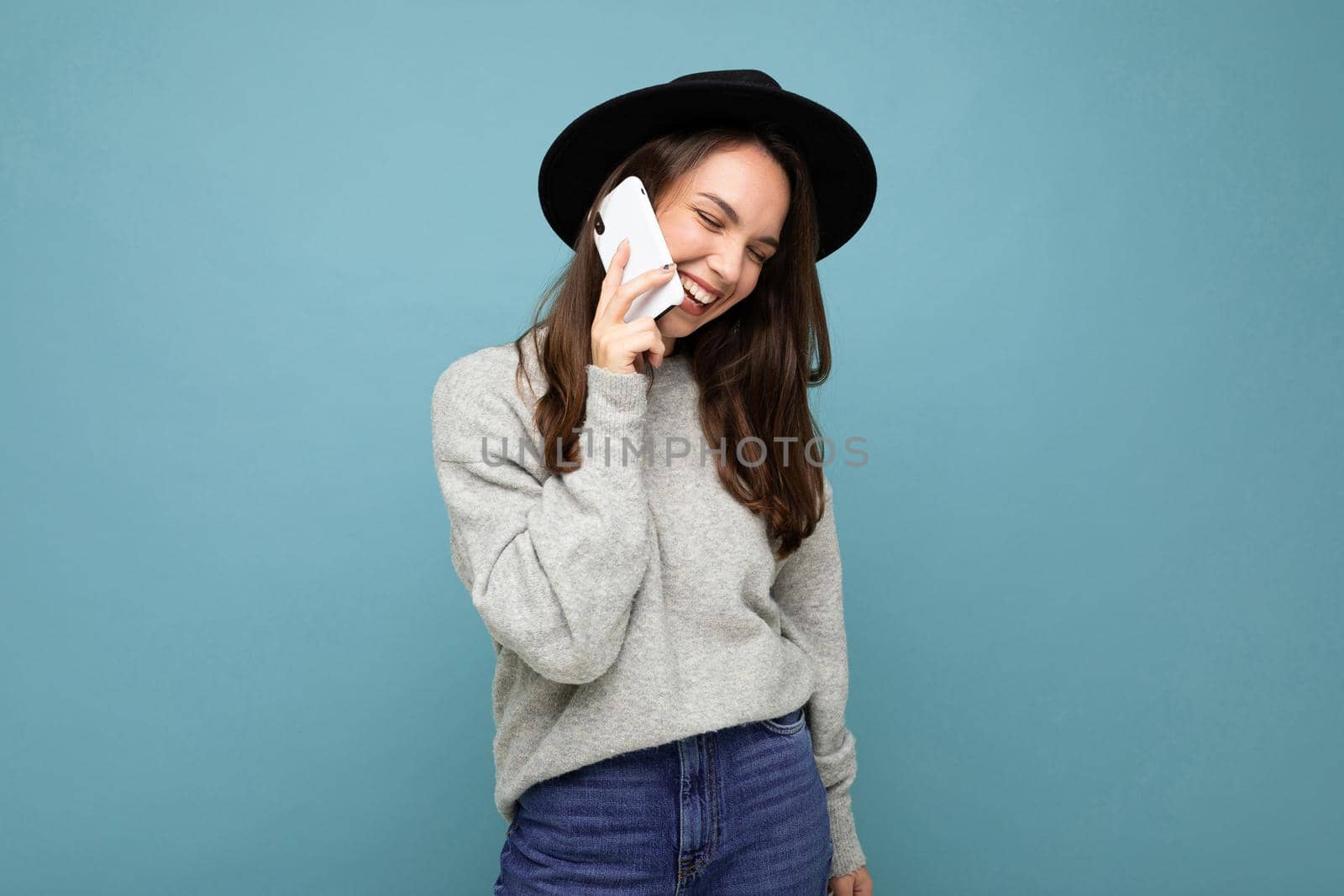 a young girl in a hat speaks on the phone against a blue wall.