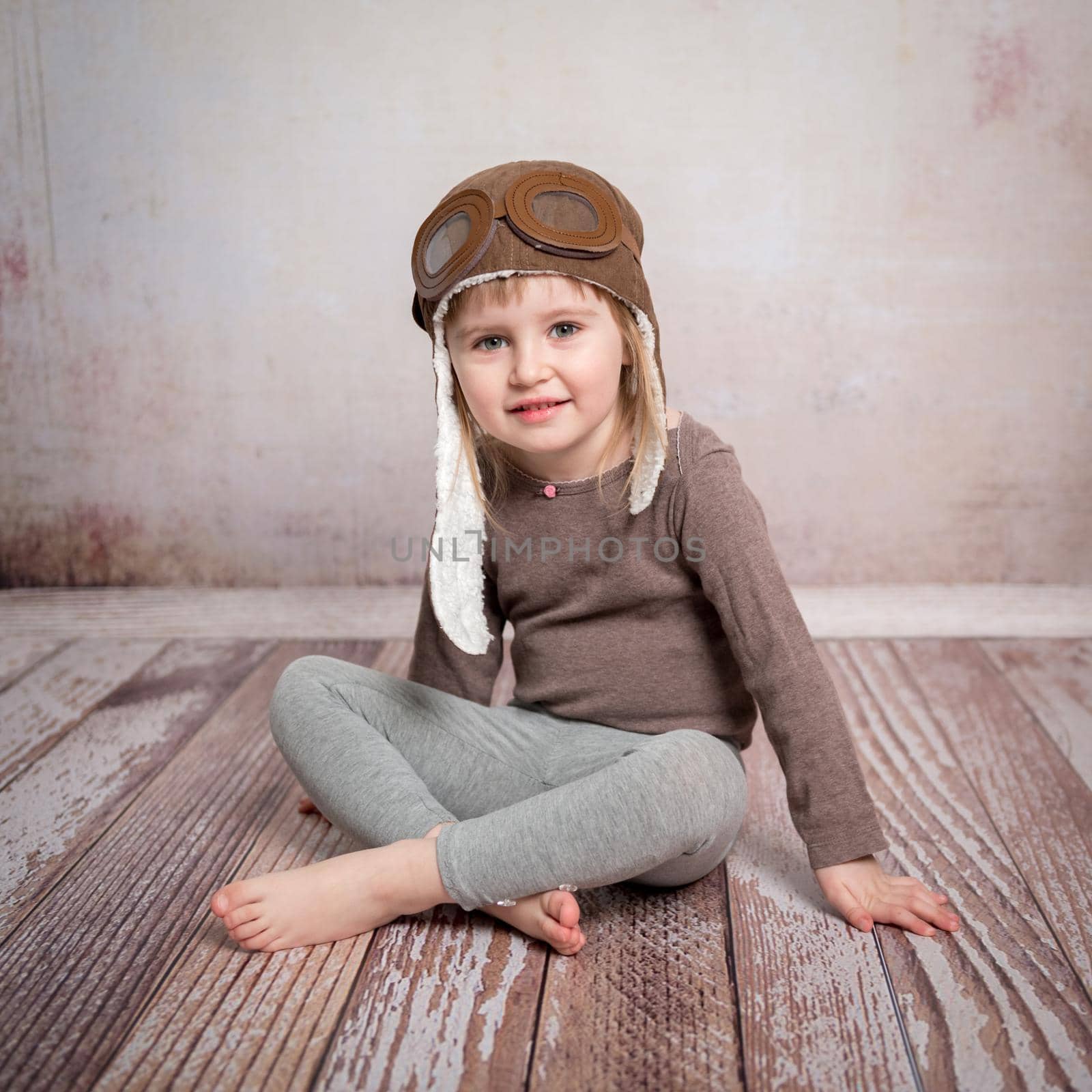 cute little girl in airman hat sitting on wooden floor