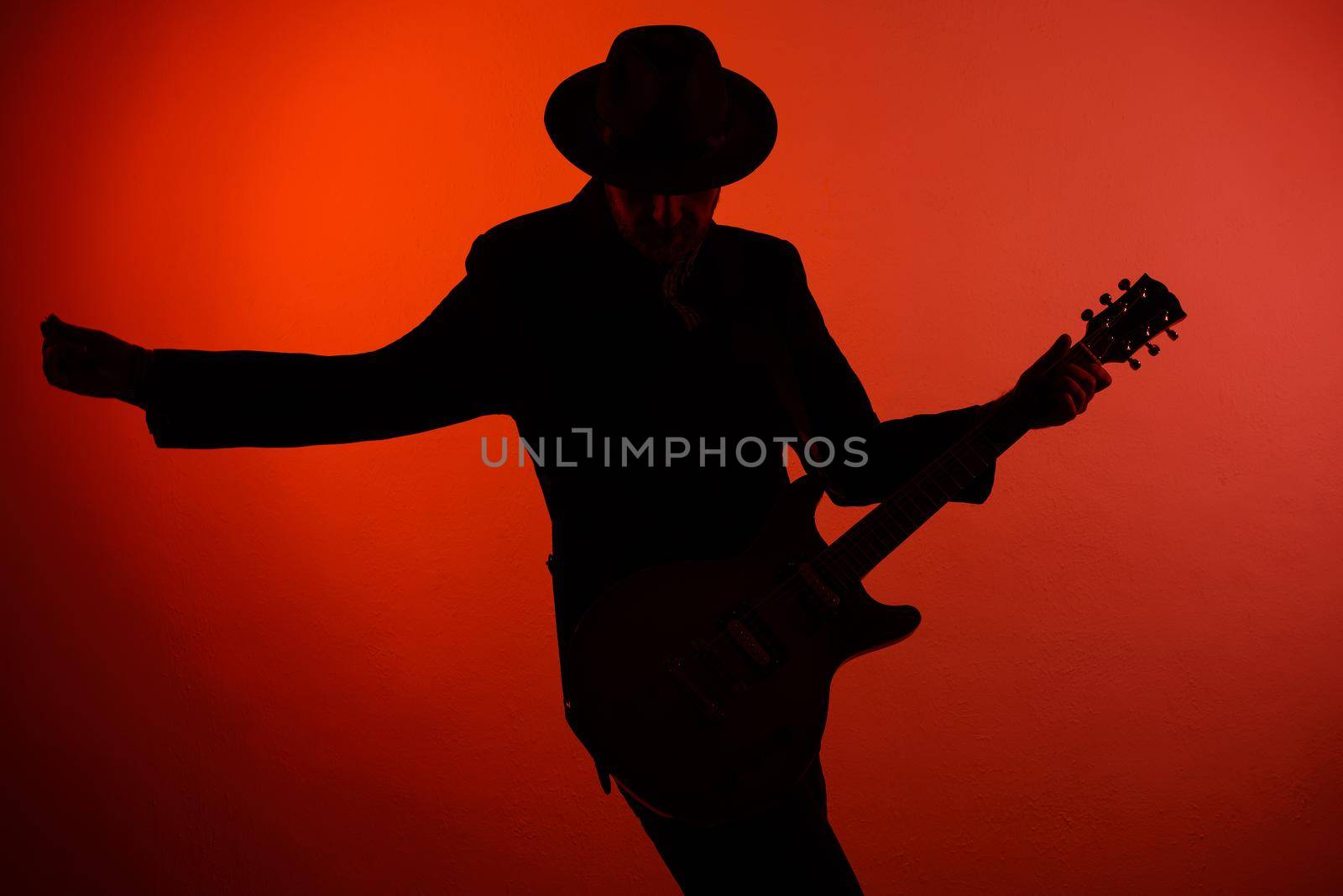 silhouette of guitarist in a hat on a red background.
