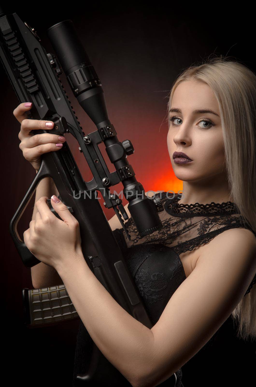 the young blonde girl in black dress posing on black background with weapon