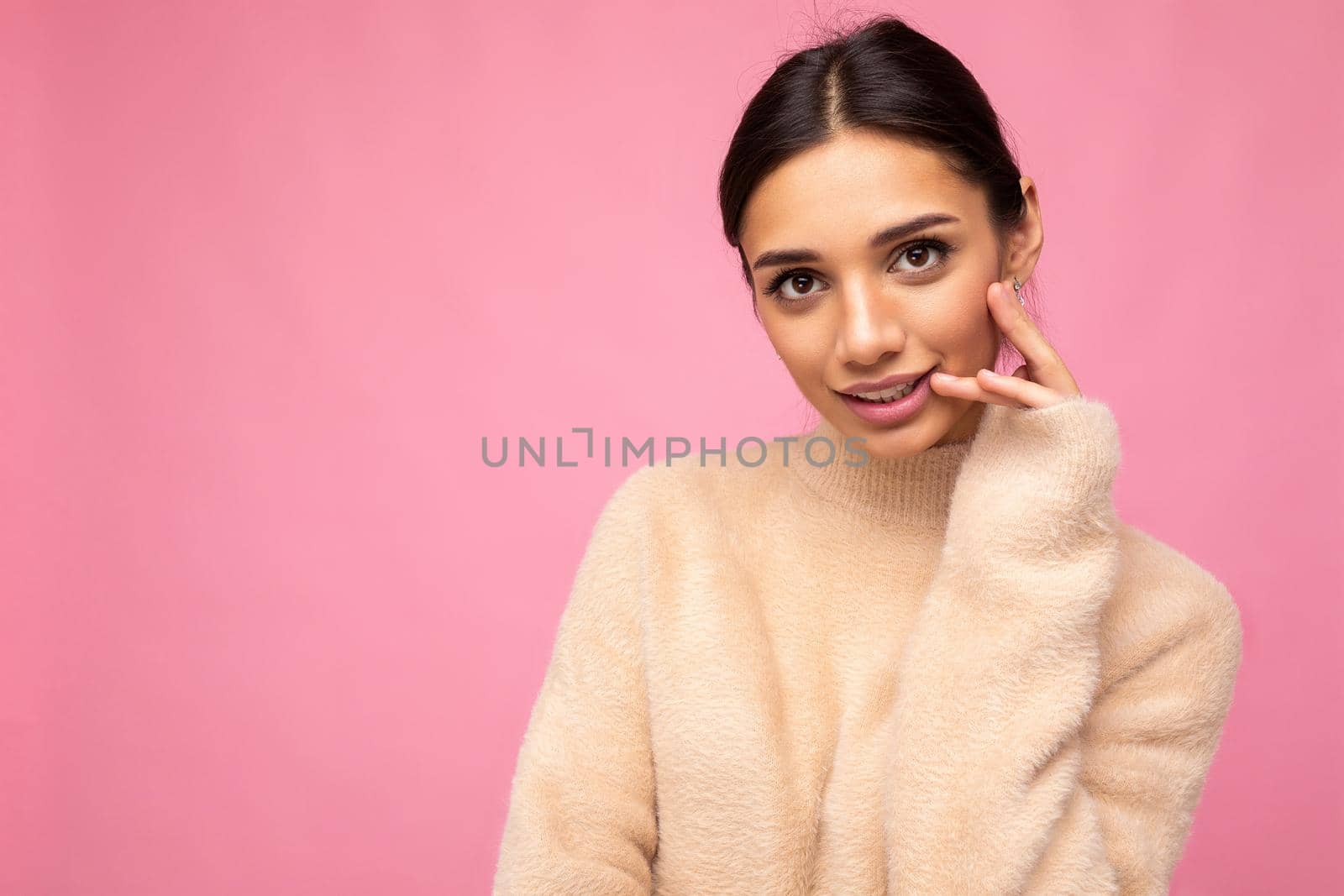 Photo of young beautiful happy cute brunette woman wearing beige jersey . Sexy carefree female person posing isolated near pink wall in studio with free space. Positive model with natural makeup.