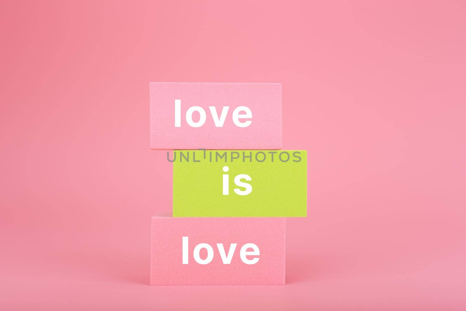 Love is love written on stack of yellow and pink rectangles on pink background. Concept of Lgbtq pride social post, tolerance, respect and equal rights