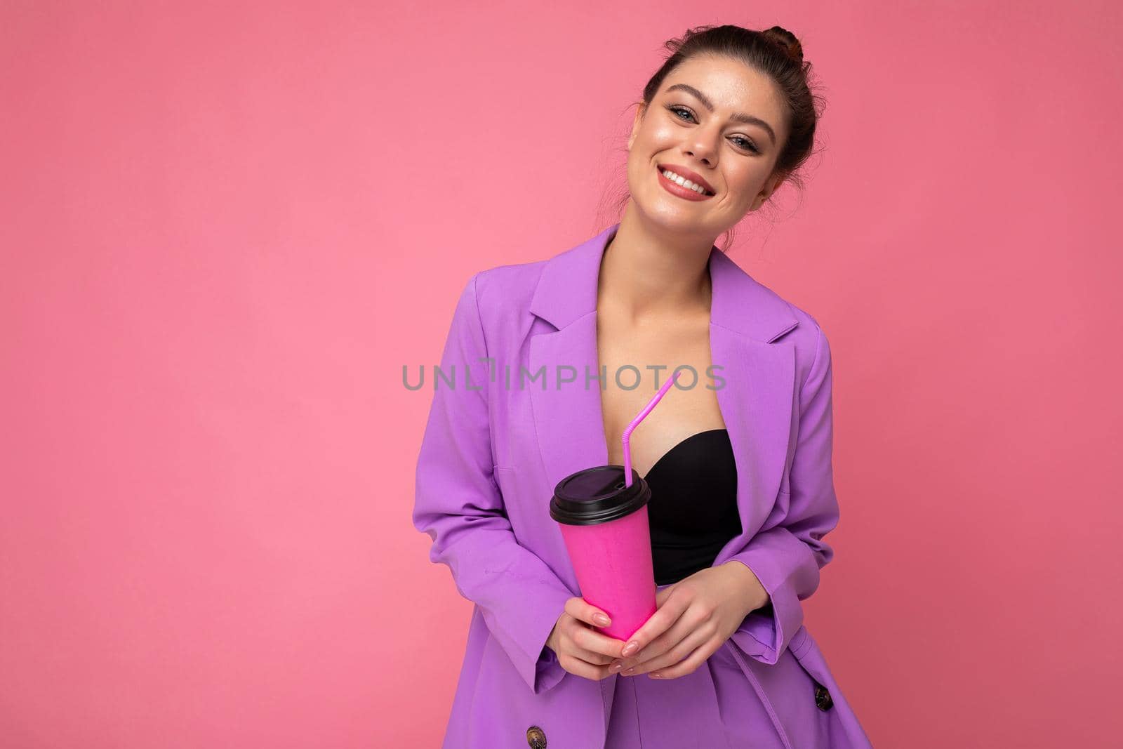 Beautiful young positive brunette woman wearing casual stylish clothes isolated over colorful background wall holding paper cup for mockup drinking coffee looking at camera. empty space