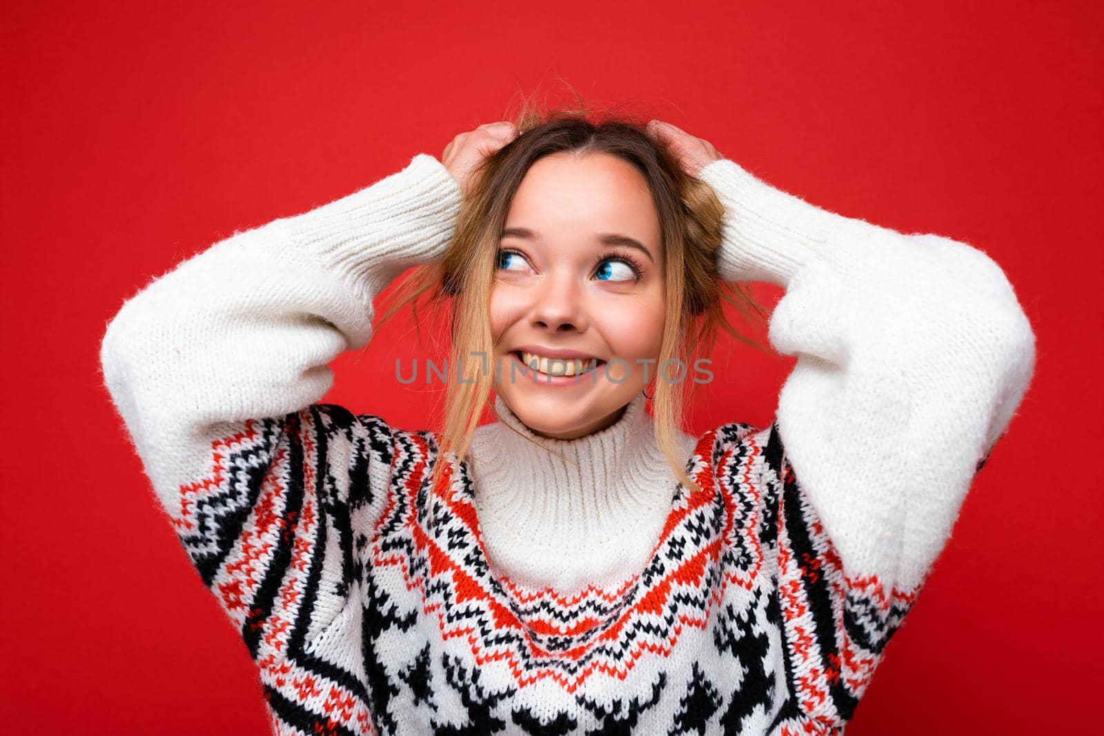 Young beautiful woman. Trendy woman in casual winter sweater. Positive female shows facial emotions. Funny model isolated on red background by TRMK