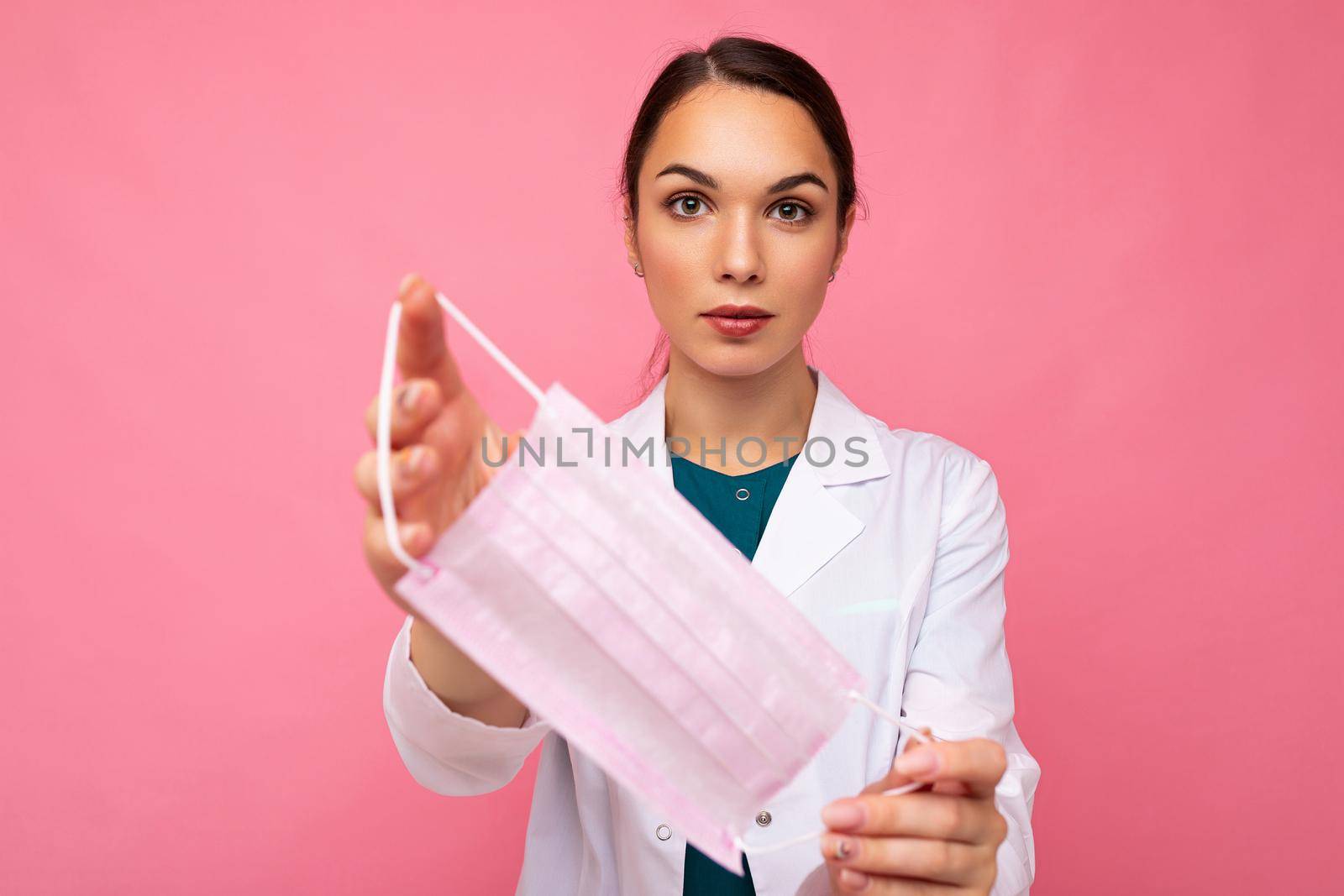 Beautiful young woman holds and wears a white medical mask to protect yourself from corona virus, cares for her health and safety, sticks to self-isolation. Concept of Covid-19.