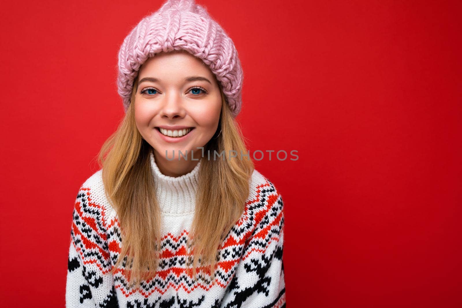 Attractive smiling happy young blonde woman standing isolated over colorful background wall wearing everyday stylish outfit showing facial emotions looking at camera.