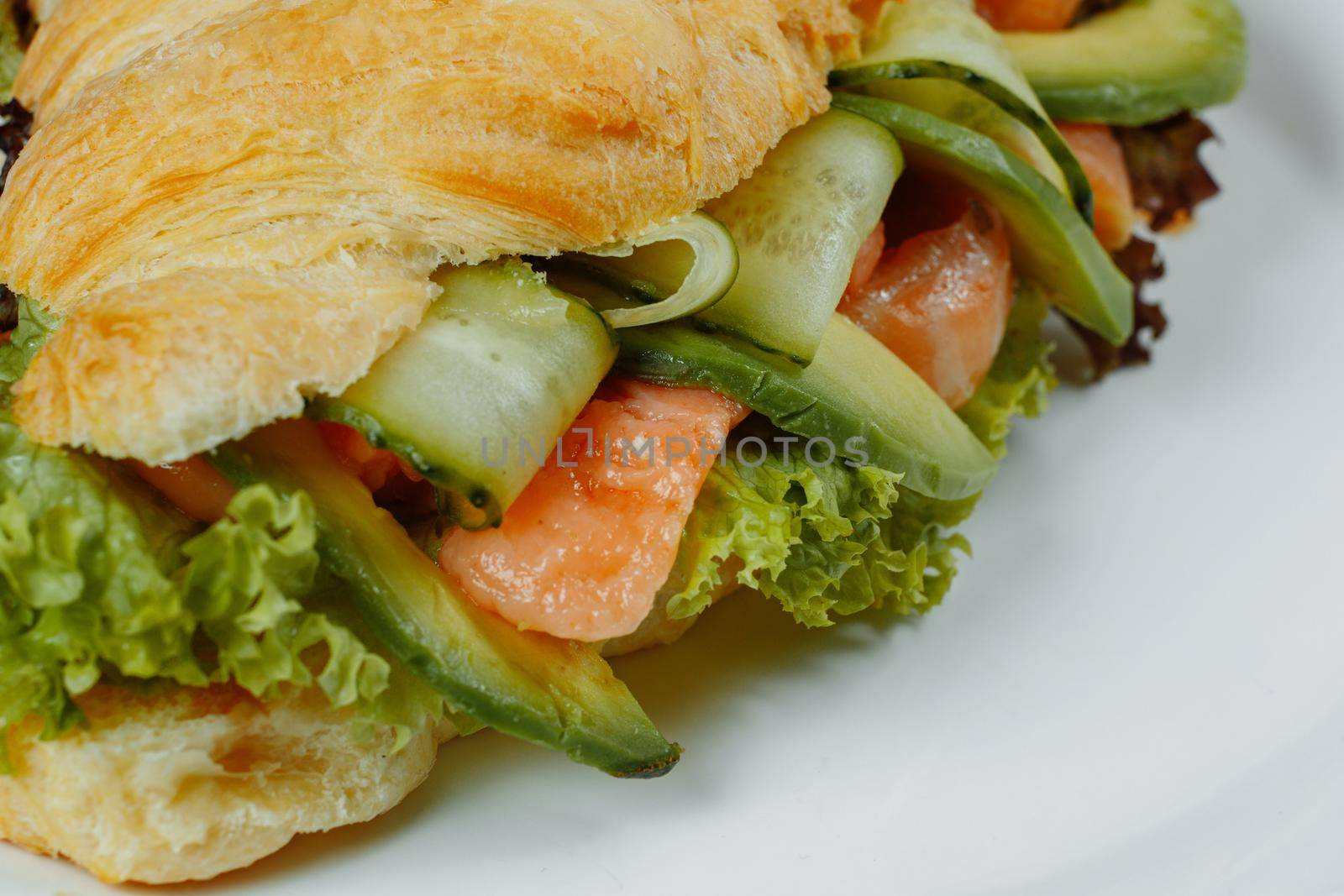Croissant sandwich with red fish, avocado, fresh vegetables and arugula on black shale board over black stone background. Healthy food concept by UcheaD