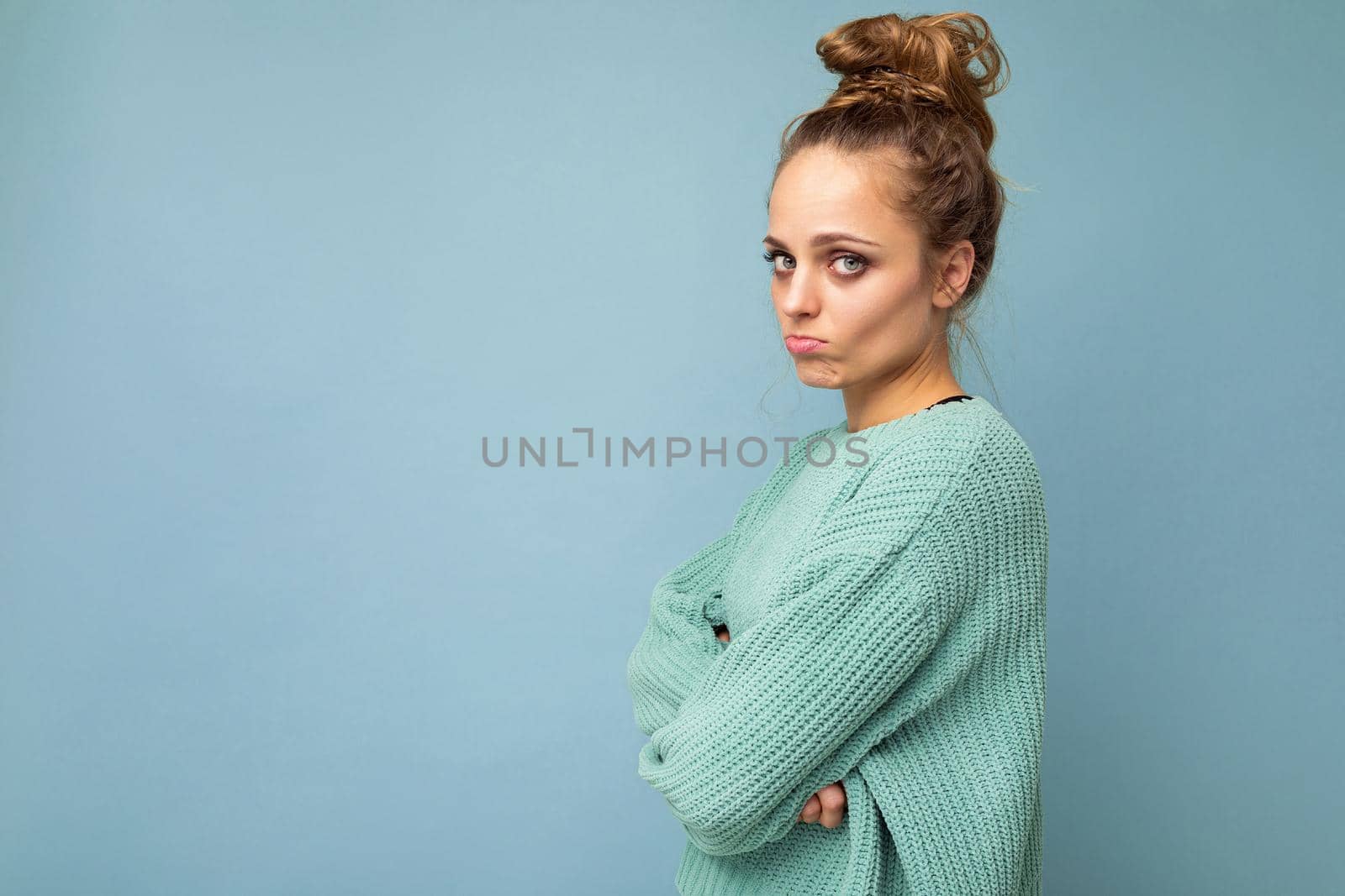 Shot of young upset touchy offended pretty blonde woman wearing blue jersey isolated on blue background with empty space.