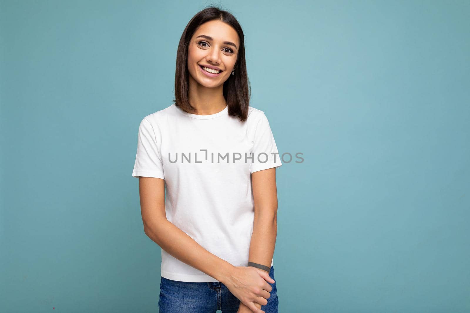 Portrait of positive cheerful fashionable smiling young brunette woman in casual white t-shirt for mockup isolated on blue background with copy space.