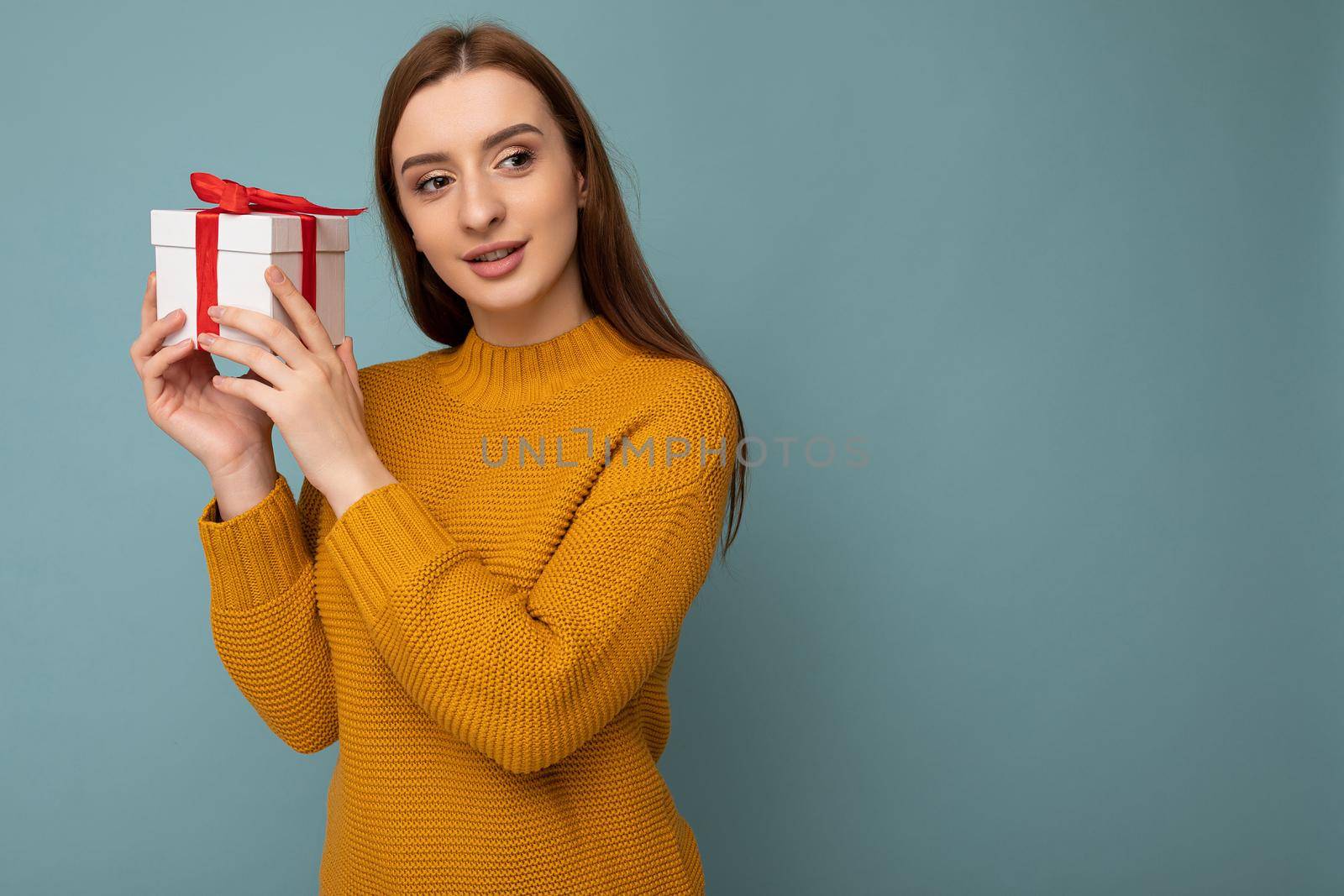 Shot of attractive positive smiling young brunette woman isolated over colourful background wall wearing everyday trendy outfit holding gift box and looking to the side. Empty space
