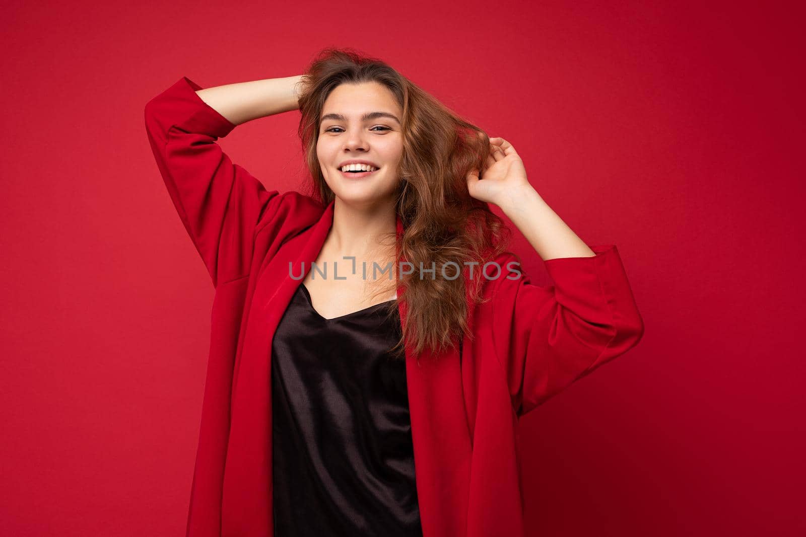 Young beautiful european stylish brunette woman wearing black blouse top and red cardigan isolated over red background with positive sincere emotions. Simple and natural looking at the camera. Free space.