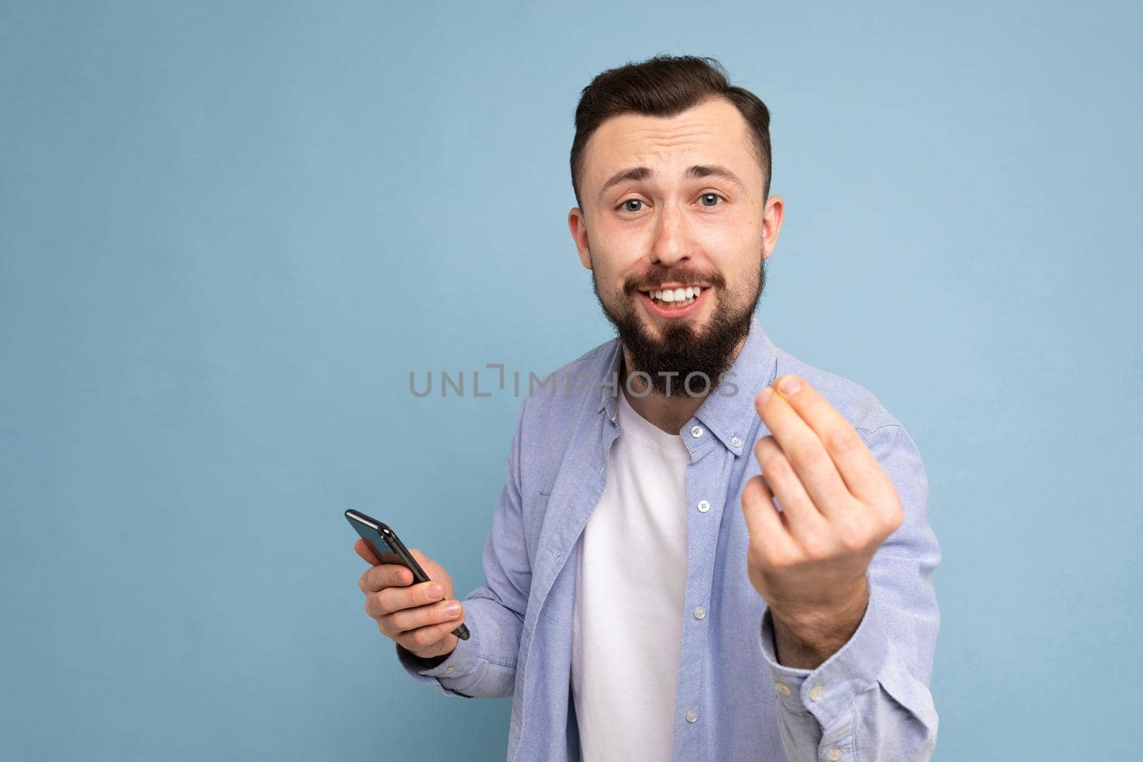 a young man with a beard on the background of a blue wall shows a gesture delicious