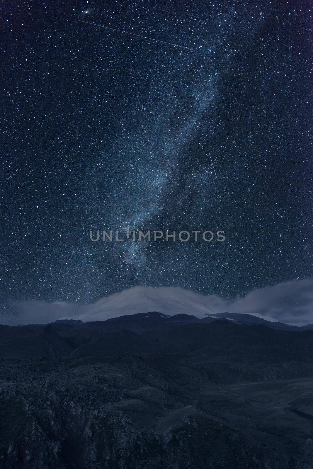 Night sky with stars and milky way over snowy mountains.