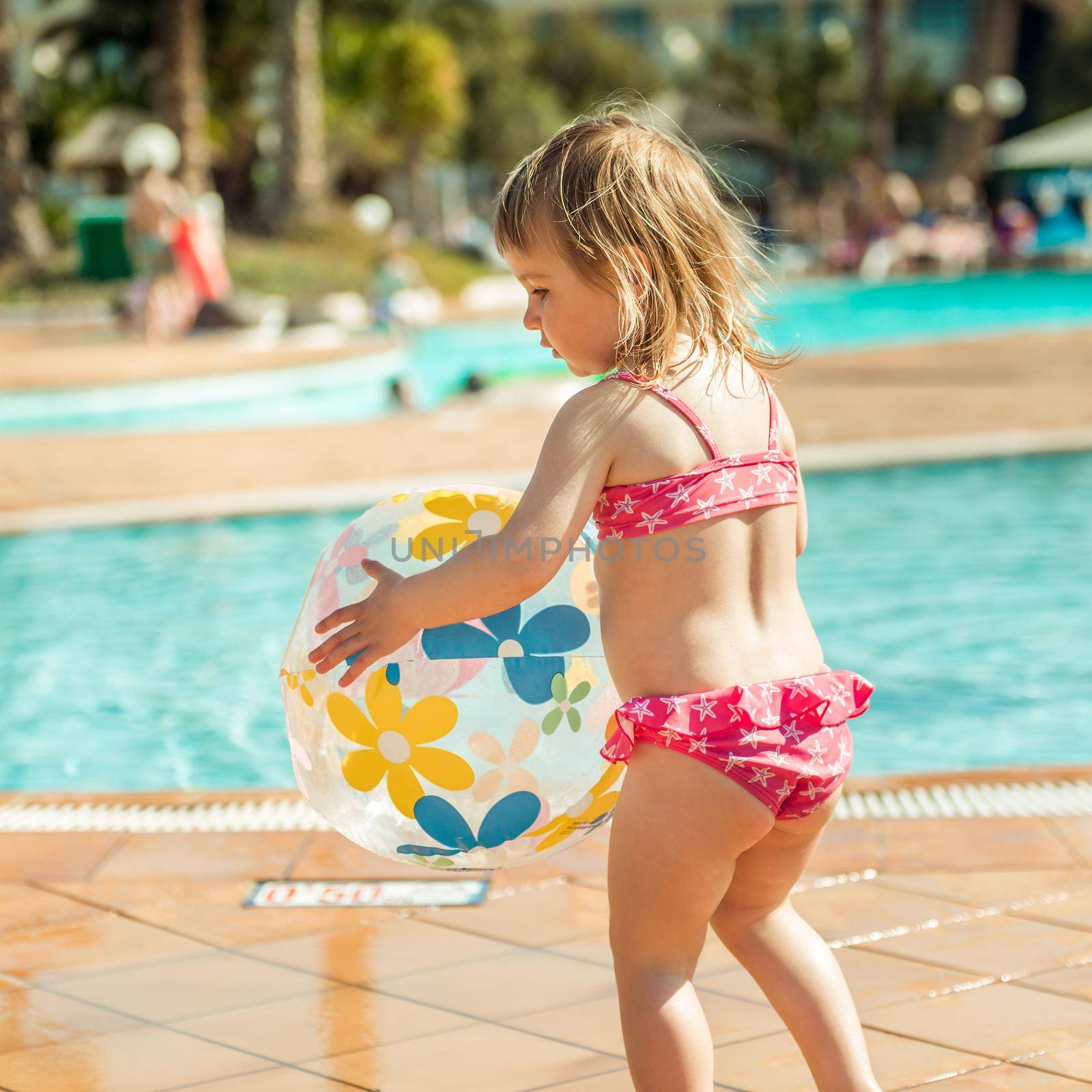 little cute girl playing near the pool with a ball