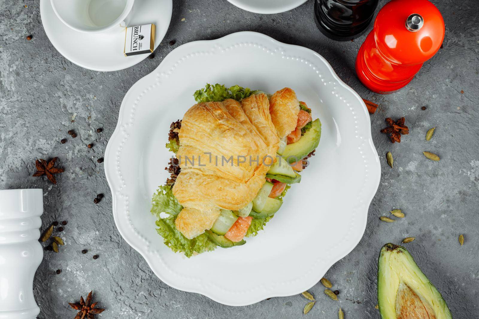 Croissant sandwich with red fish, avocado, fresh vegetables and arugula on black shale board over black stone background. Healthy food concept by UcheaD