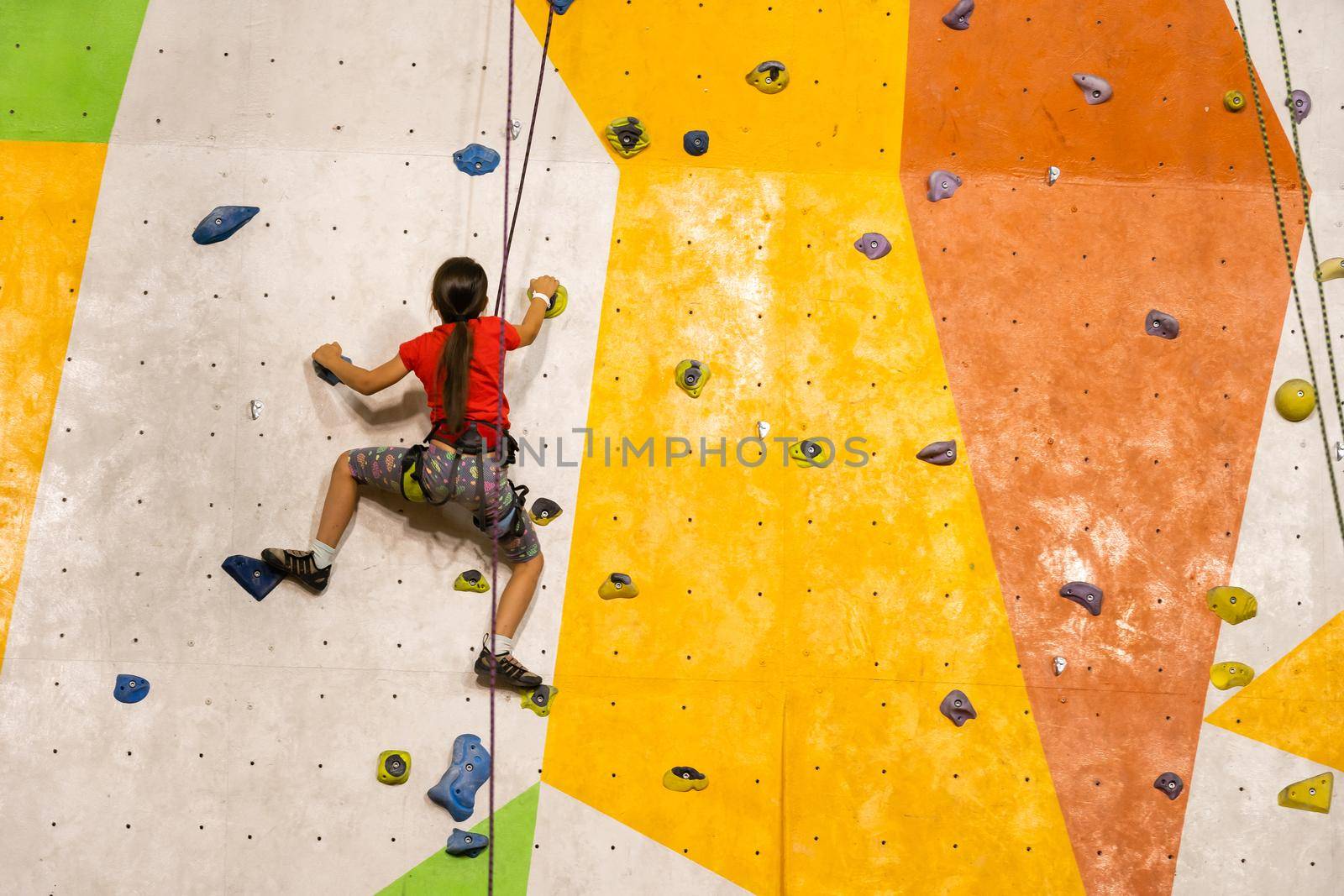 Sporty little girl climbing artificial boulder on practical wall in gym