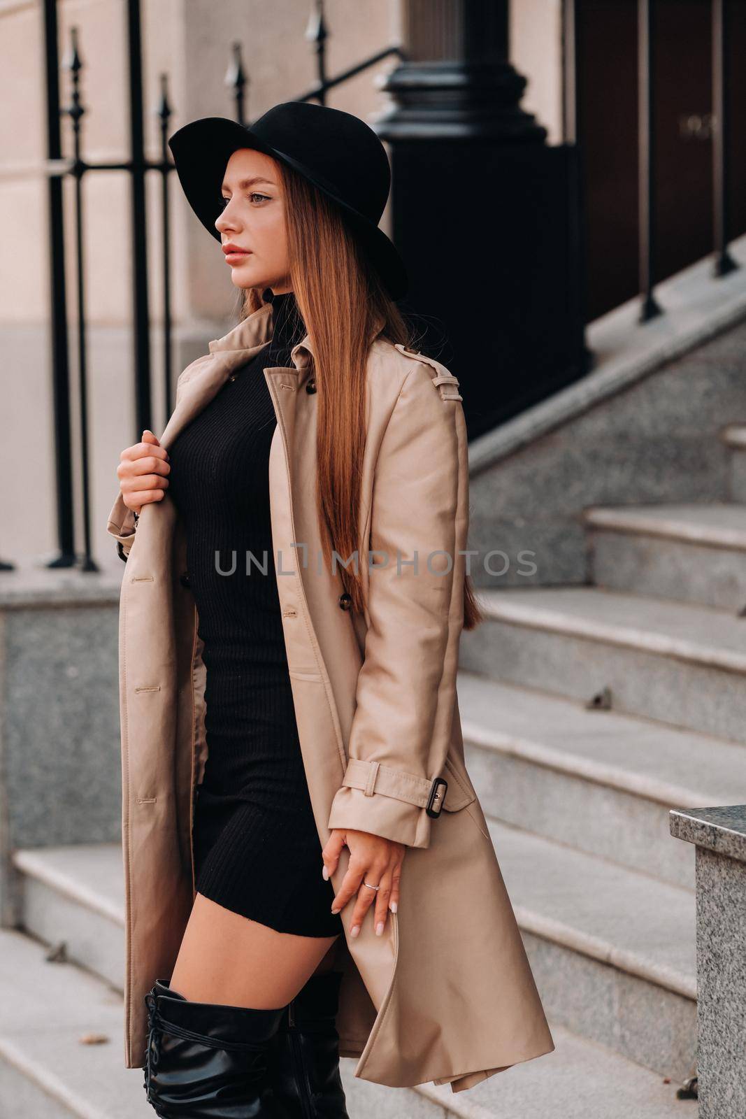 Stylish young woman in a beige coat in a black hat on a city street. Women's street fashion. Autumn clothing.Urban style.