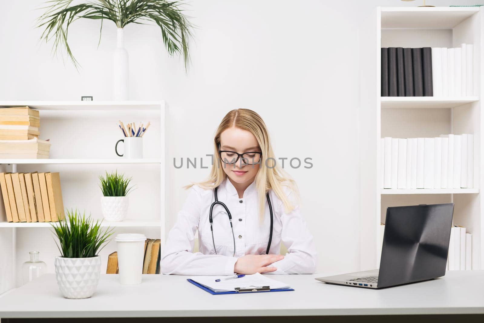 Young beautiful doctor woman working happy and smile in hospital, sitting on table, medical concept