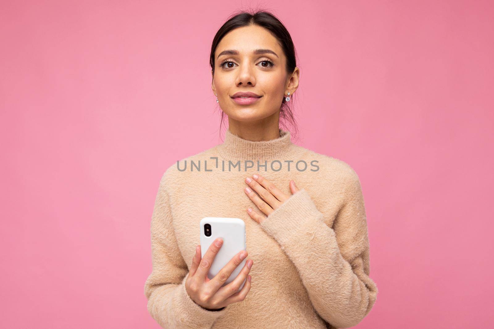 portrait of a gentle brunette on a pink background. holding a phone, looking at the camera by TRMK