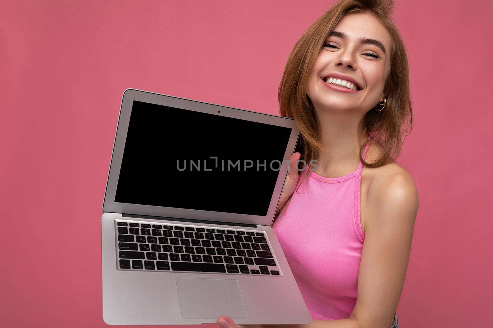 Photo of smiling funny cute beautiful young woman holding netbook looking at camera isolated over colourful background. Copy space, empty monitor