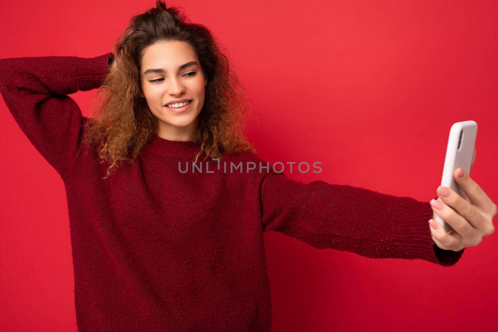 Attractive charming young smiling happy woman holding and using mobile phone taking selfie wearing stylish clothes isolated over wall background.