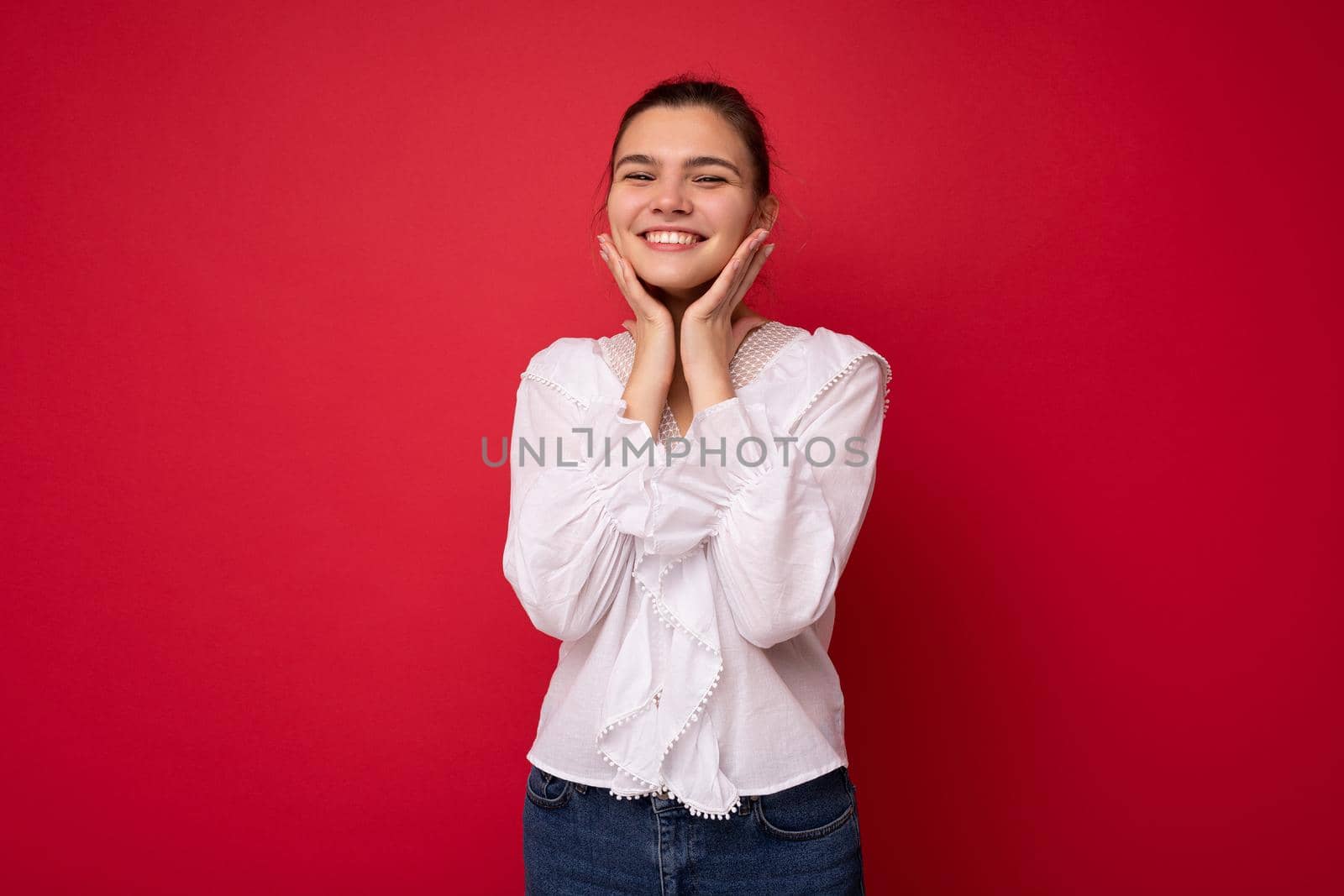 Photo portrait of charming happy funny young brunette woman in stylish white blouse. Sexy carefree female person posing isolated on red background. Positive model shows sincere emotions.