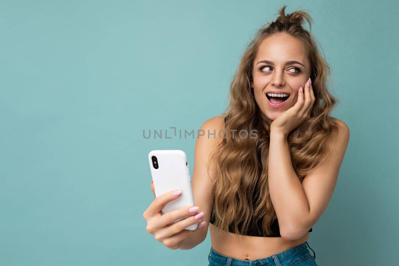 Photo of attractive crazy amazed surprised young woman wearing casual stylish clothes standing isolated over background with copy space holding and using mobile phone looking to the side.