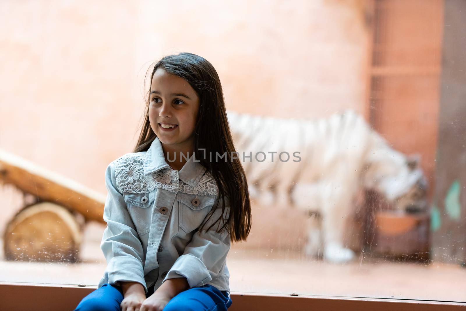 little girl and white tiger behind glass at the zoo