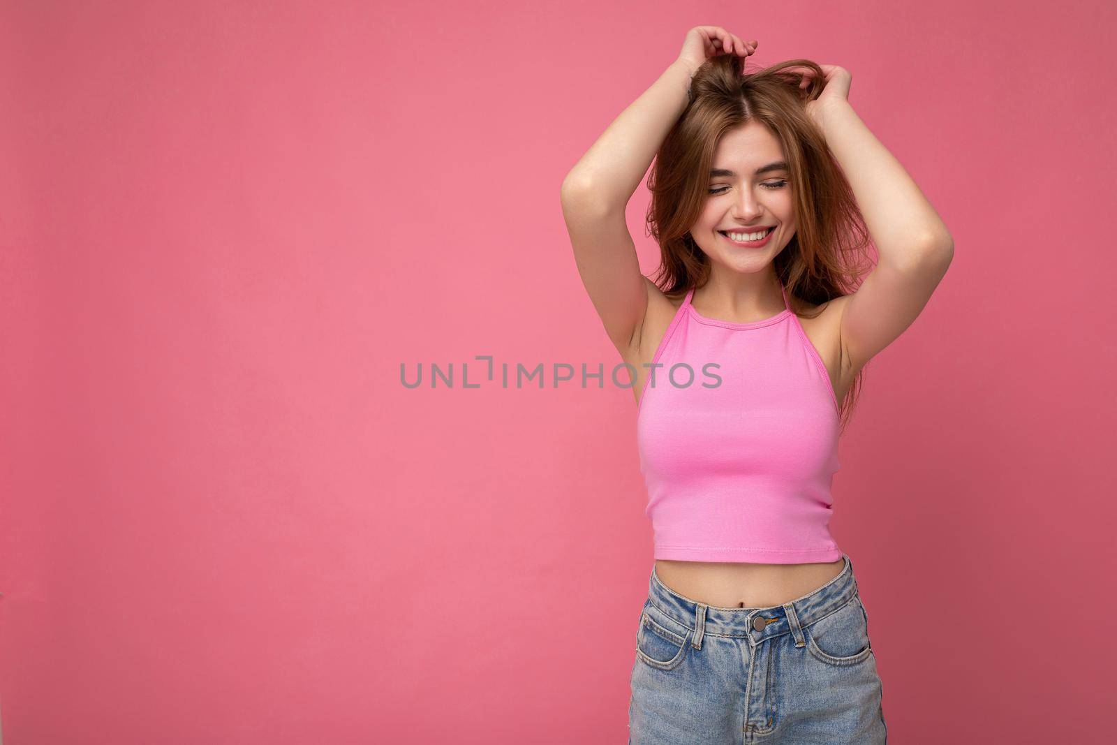 Young smiling beautiful dark blonde woman with sincere emotions isolated on background wall with copy space wearing stylish pink top. Positive concept.