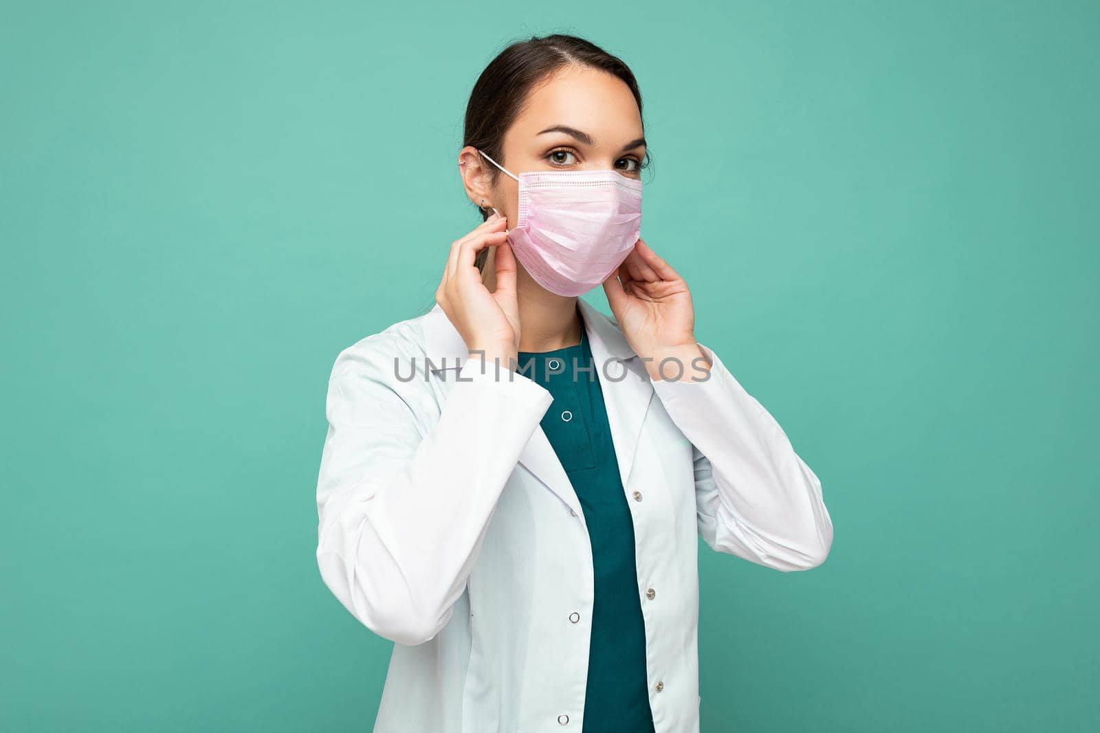 Beautiful young woman holds and wears a white medical mask to protect yourself from corona virus, cares for her health and safety, sticks to self-isolation. Concept of Covid-19.