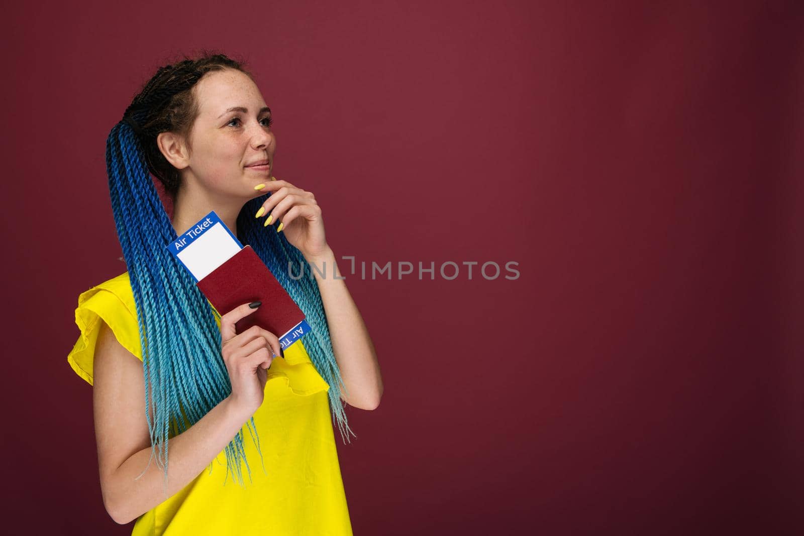 A modern trendy smiling woman in yellow dress with air tickets and a passport in her hand. Young dreamy girl looks aside up. Travel concept