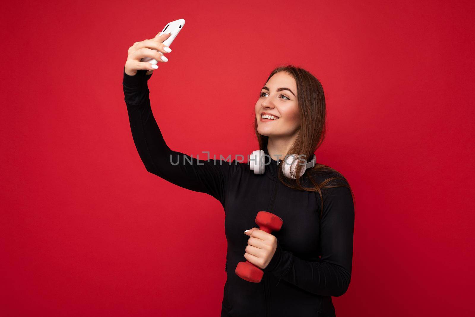 Attractive charming young smiling happy woman holding and using mobile phone taking selfie wearing stylish clothes isolated over wall background.