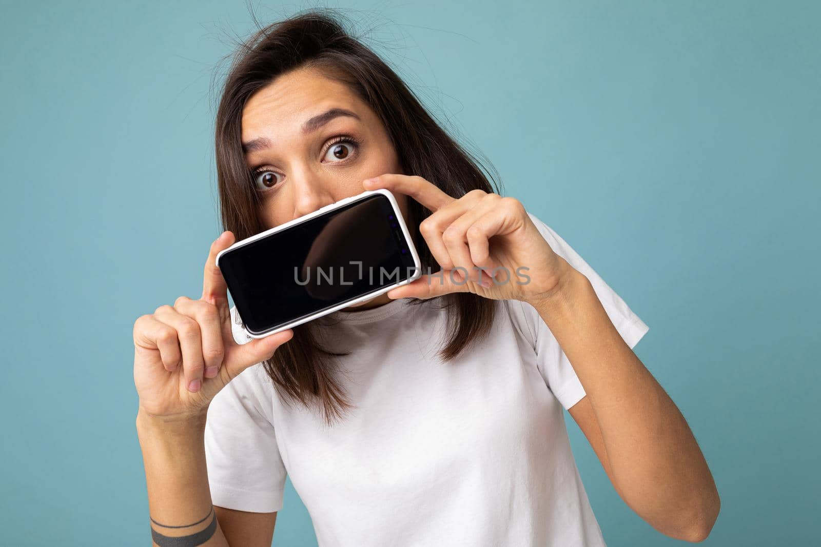 Image of a shocked young beautiful woman posing isolated over blue wall background play games by mobile phone. by TRMK