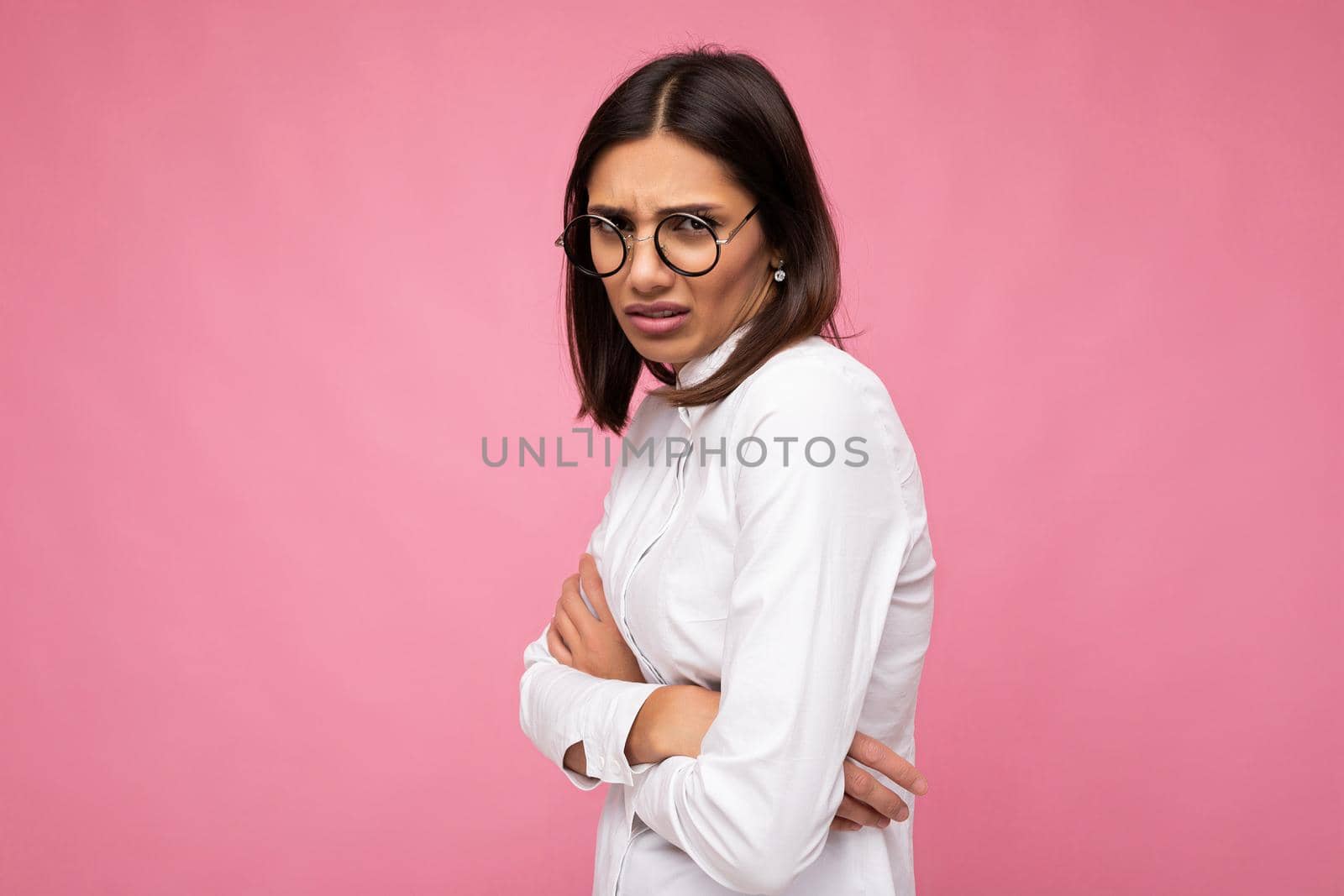 Attractive young offended sad brunette woman wearing everyday stylish clothes and modern optical glasses isolated on colorful background wall looking at camera.