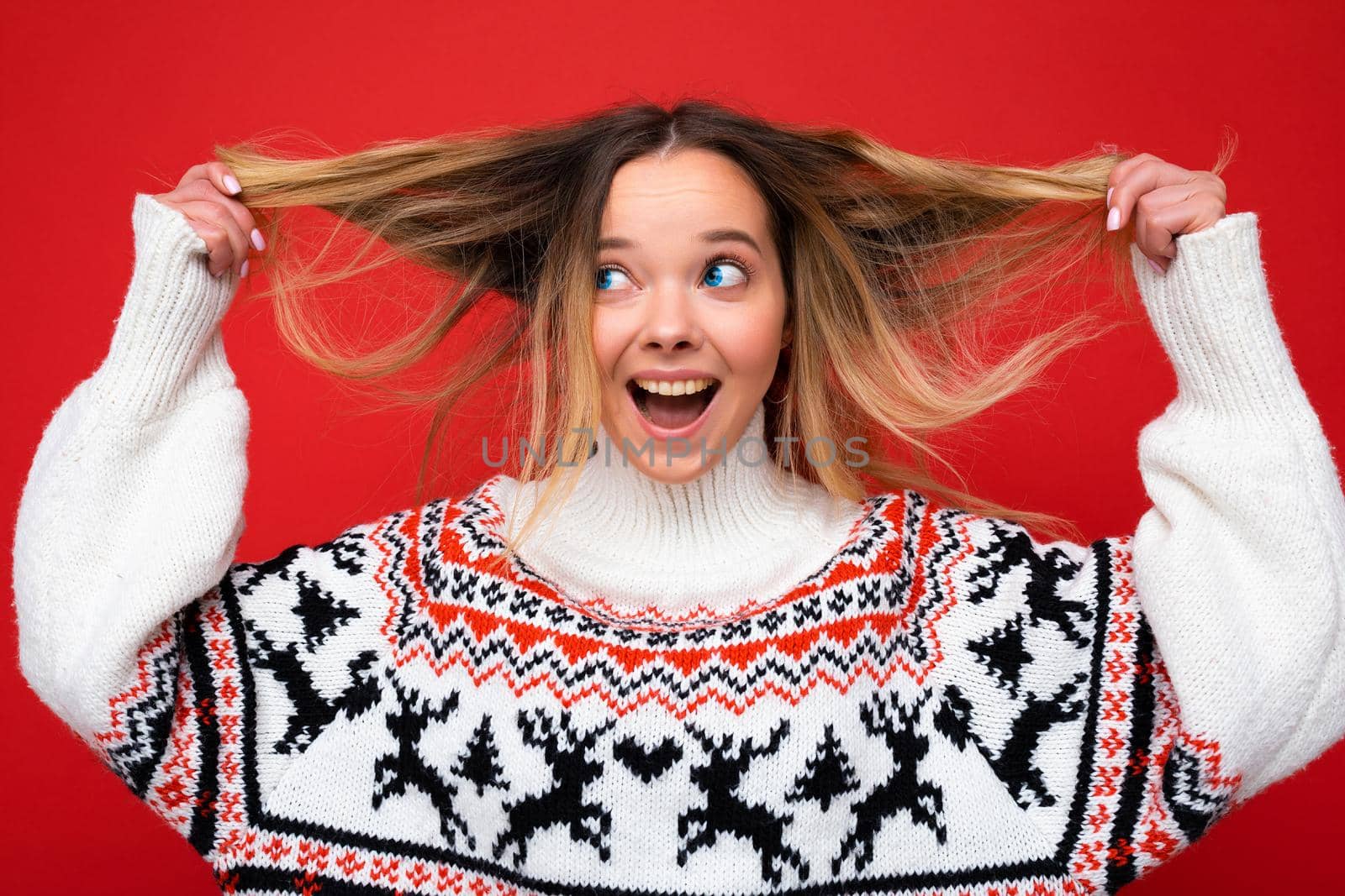 Young beautiful woman. Trendy woman in casual winter sweater. Positive female shows facial emotions. Funny model isolated on red background by TRMK