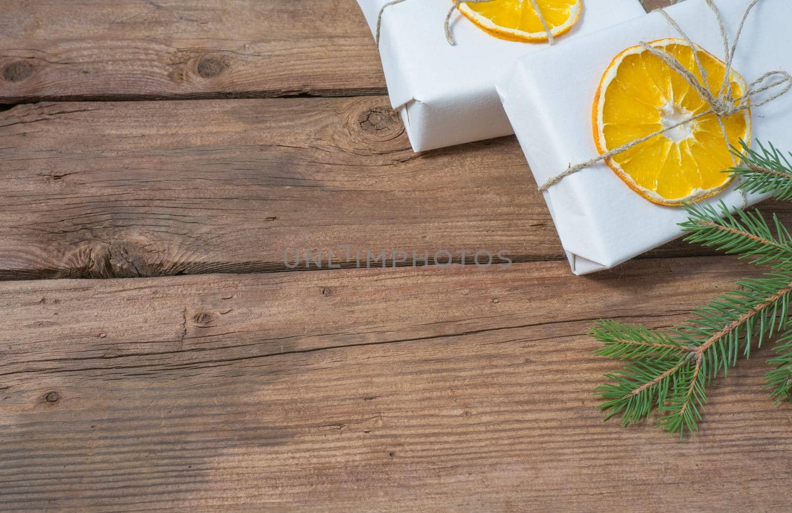 Christmas presents or gift box wrapped in kraft paper with decorations, pine cones, dried orange orange slices and fir branches on a rustic wooden background. Holiday concept