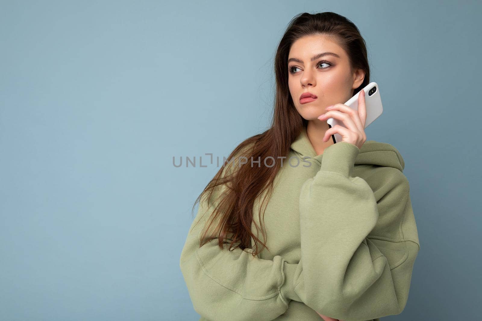 serious upset attractive young woman wearing stylish hoodie holding using mobile phone isolated on background looking to the side.Copy space