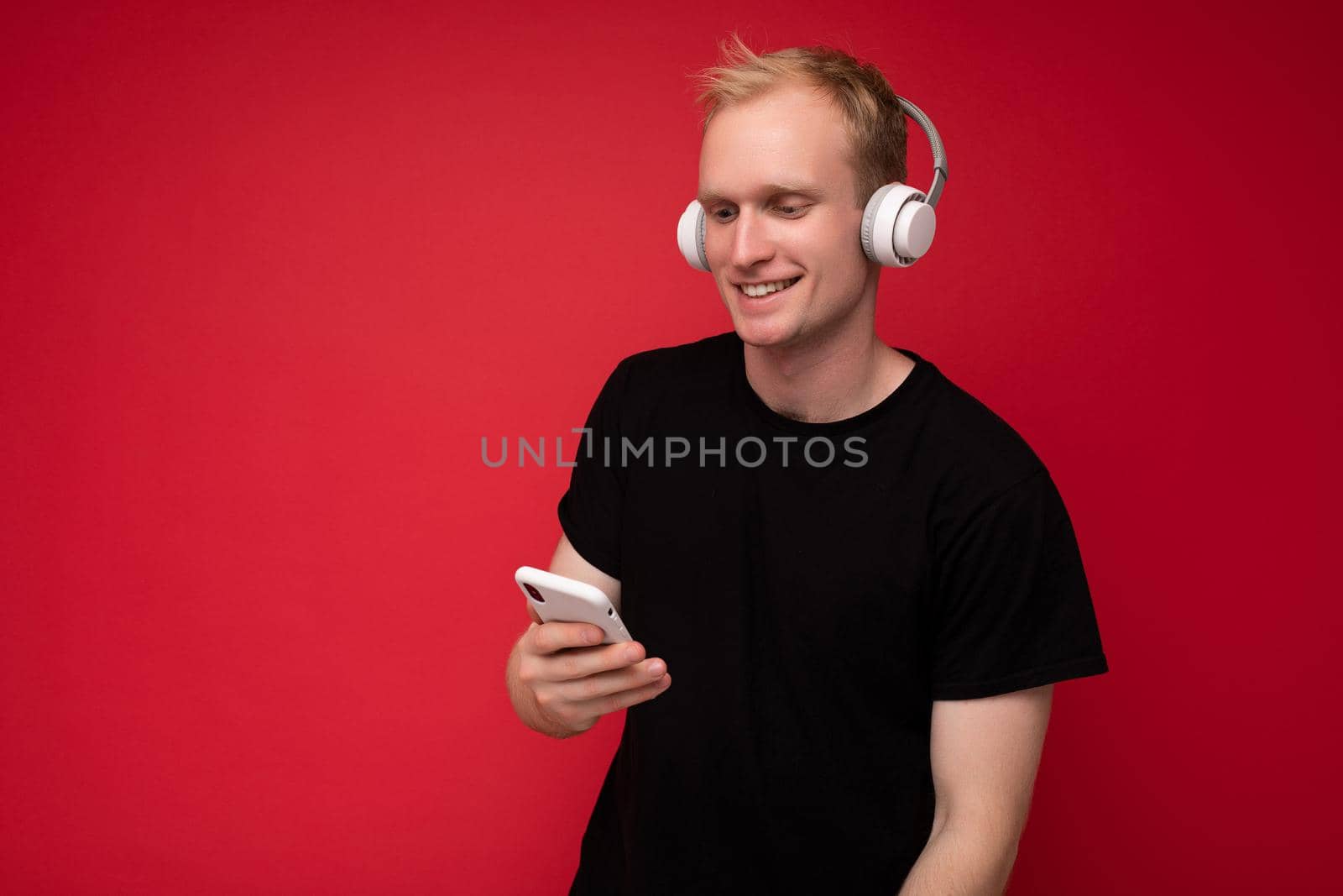 Photo shot of handsome positive good looking young man wearing casual stylish outfit poising isolated on background with empty space holding in hand and using mobile phone messaging sms looking at smartphone display screen.