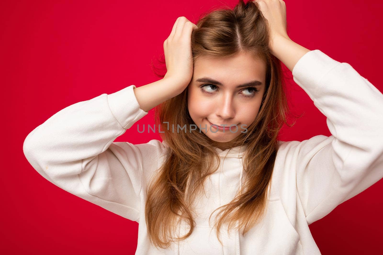 Young emotional crazy beautiful dark blonde woman with sincere emotions isolated on background wall with copy space wearing casual white hoodie. Feelings concept.