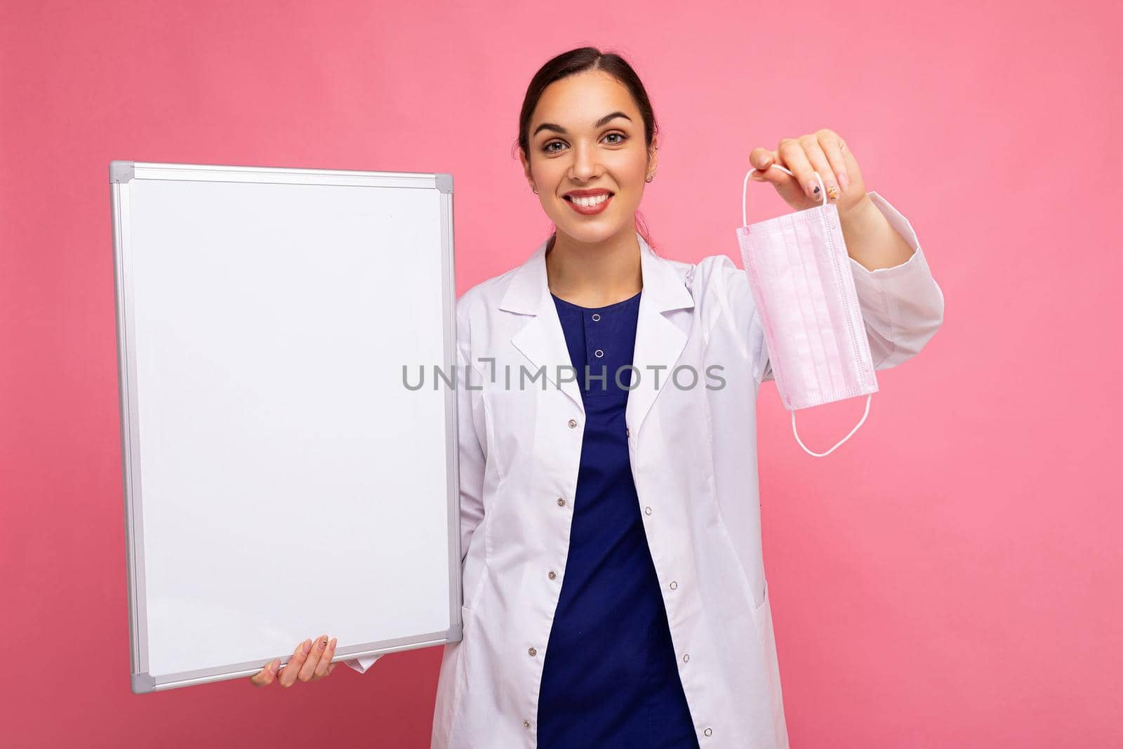 Woman doctor in a white medical coat holding blank board with copy space for text and protective mask isolated on background. Covid concept.