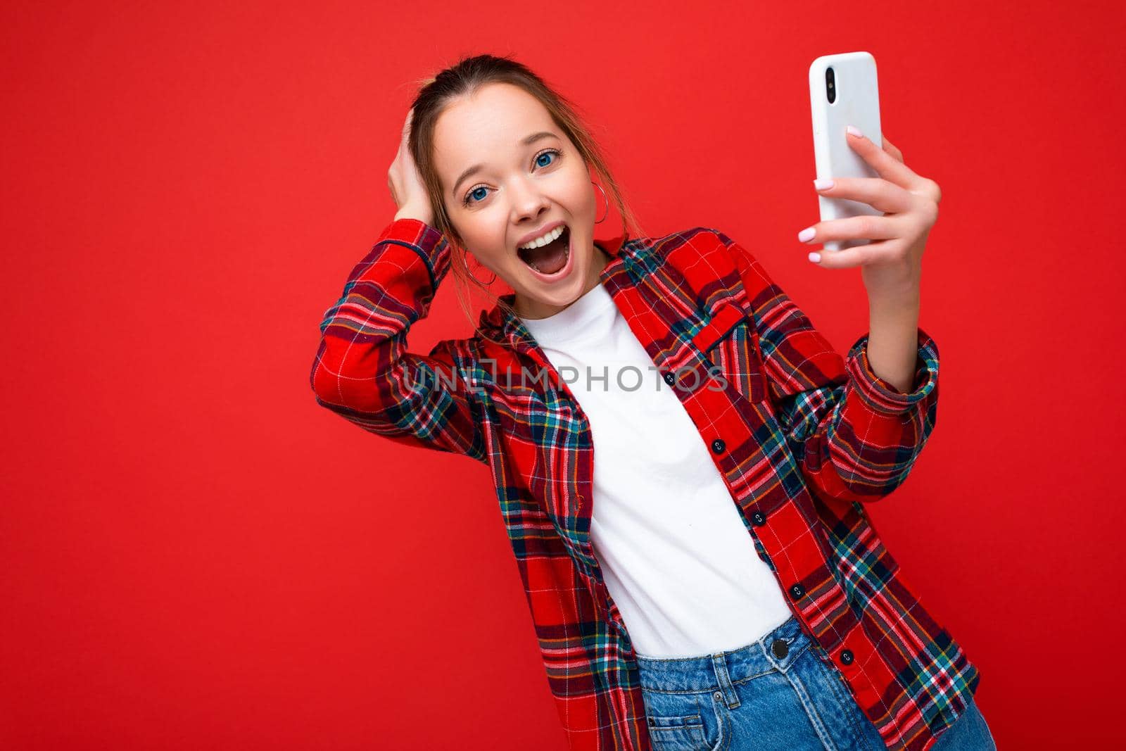 Photo of attractive crazy amazed surprised young woman wearing casual stylish clothes standing isolated over background with copy space holding and using mobile phone looking at camera.