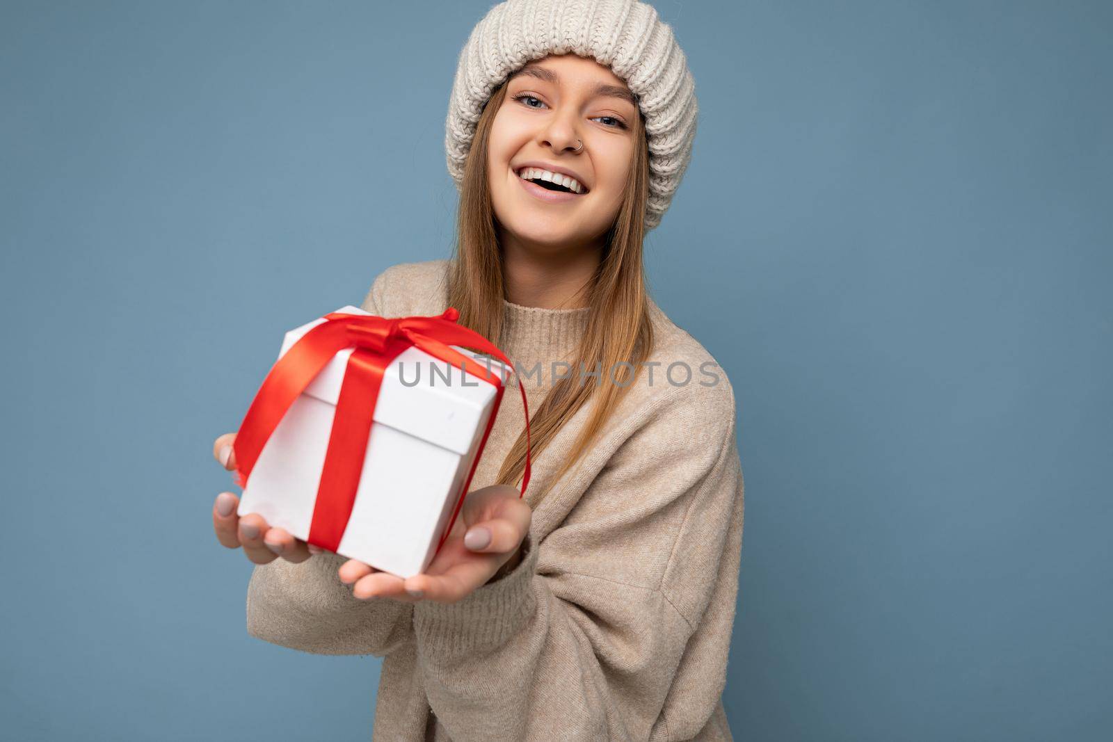 Shot of attractive positive smiling young dark blonde woman isolated over colourful background wall wearing everyday trendy outfit holding gift box and looking at camera. Copy space, mockup