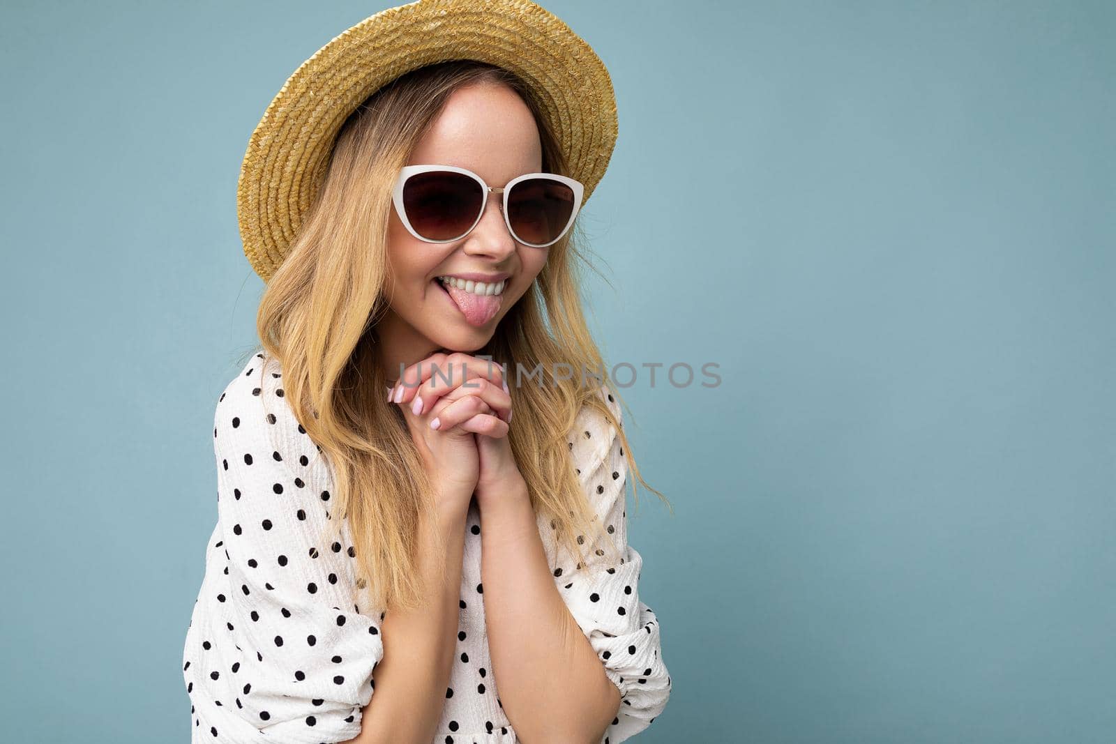 Side-profile photo of attractive positive happy young blonde woman wearing everyday stylish clothes and modern sunglasses isolated on colorful background wall looking to the side and showing tongue. copy space