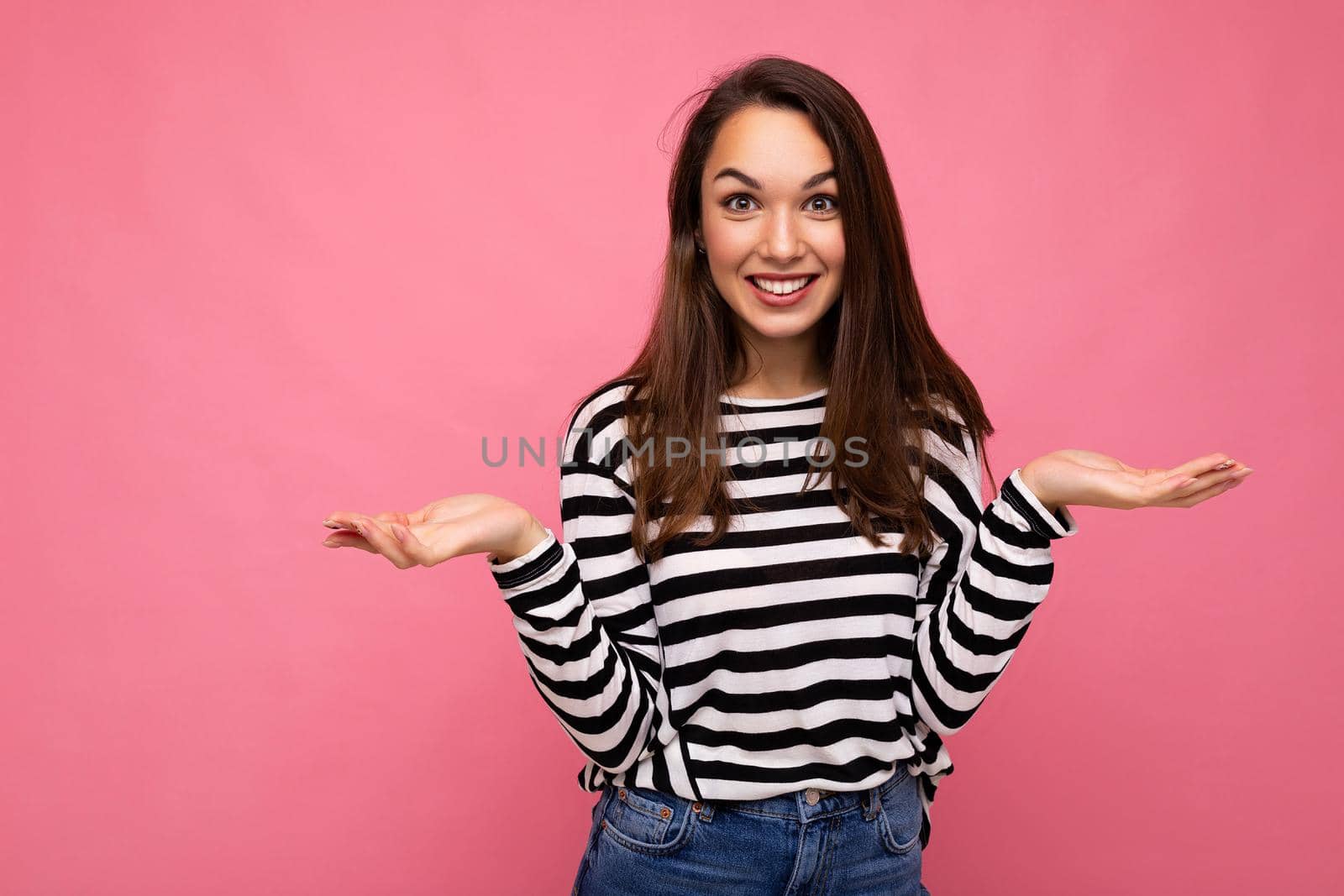 Photo of young positive happy beautiful brunette woman with sincere emotions wearing casual striped pullover isolated on pink background with copy space by TRMK