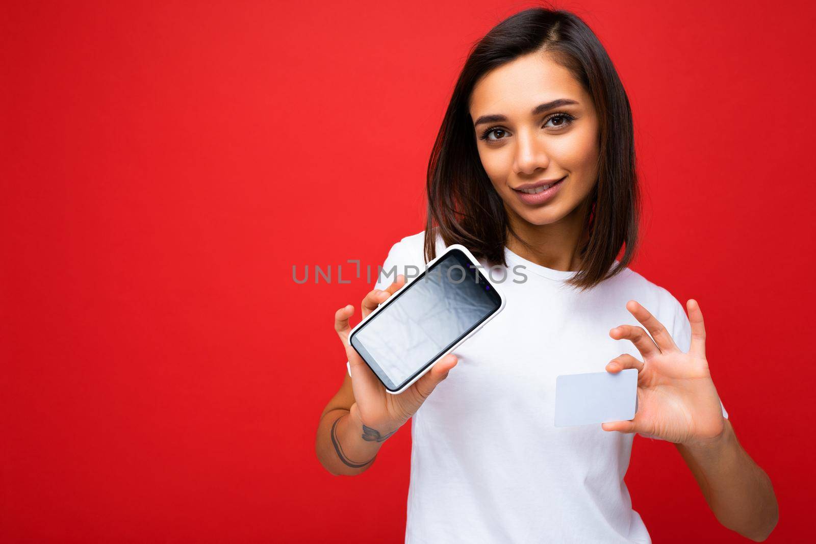 Photo of beautiful smiling young woman good looking wearing casual stylish outfit standing isolated on background with copy space holding smartphone showing phone in hand with empty screen display for mockup looking at camera.