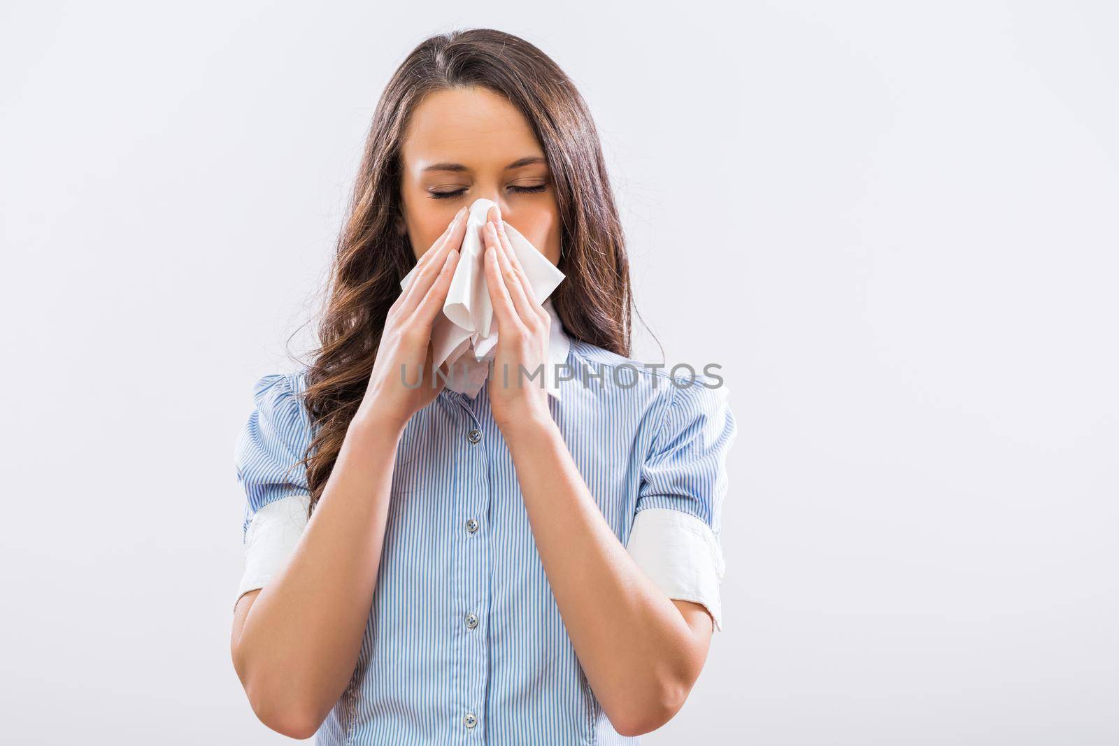 Image of businesswoman blowing nose on gray background.