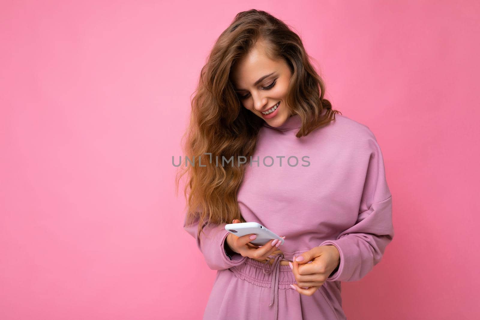 beautiful young blonde woman happy woman wearing casual clothes standing isolated over background surfing on the internet via phone looking at mobile screen.
